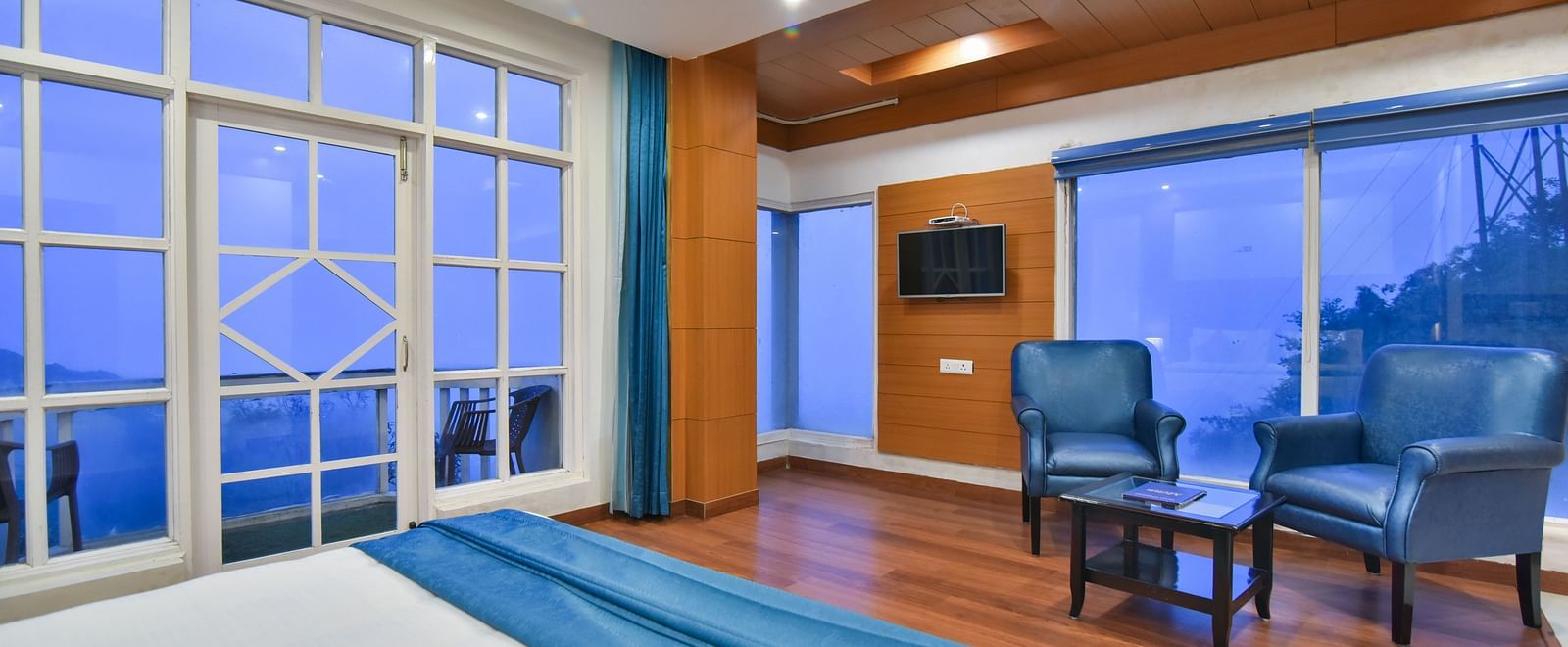View from the bed of two comfortable chairs next to TV in Luxury Room with Balcony at DLS Highland Resort and Spa, Mussoorie.